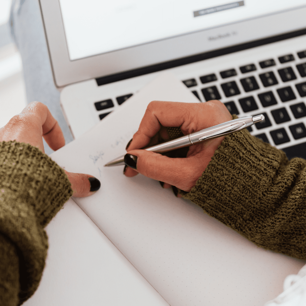 Woman writing in a notebook with a laptop in the background