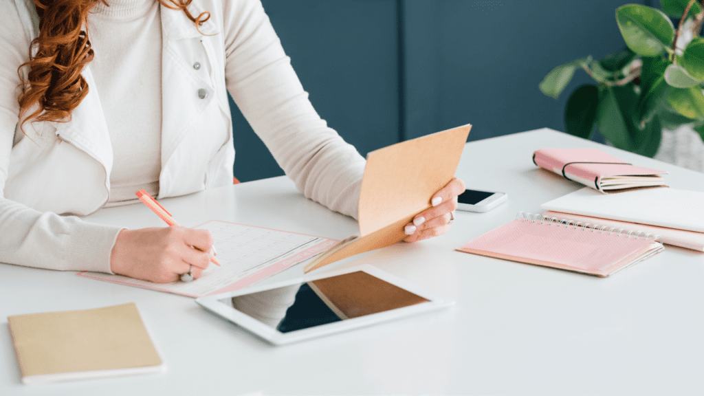 Woman writing at desk with with iPad on the table