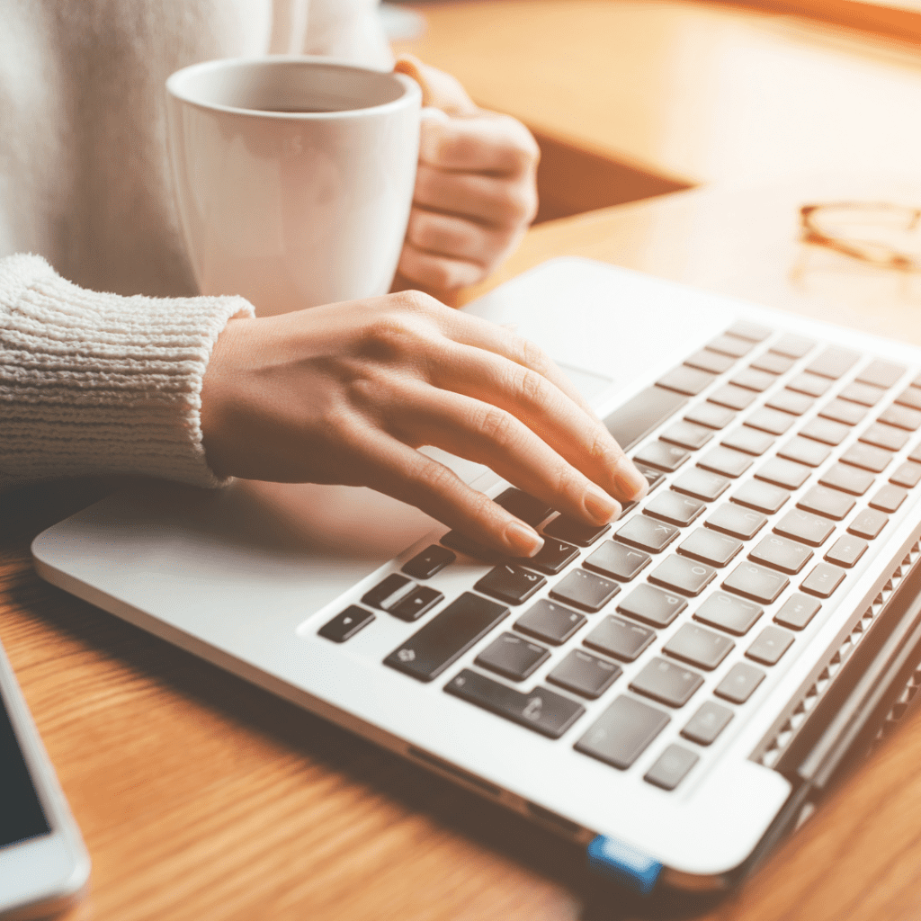 Woman working on laptop with a cup of coffee in her other hand