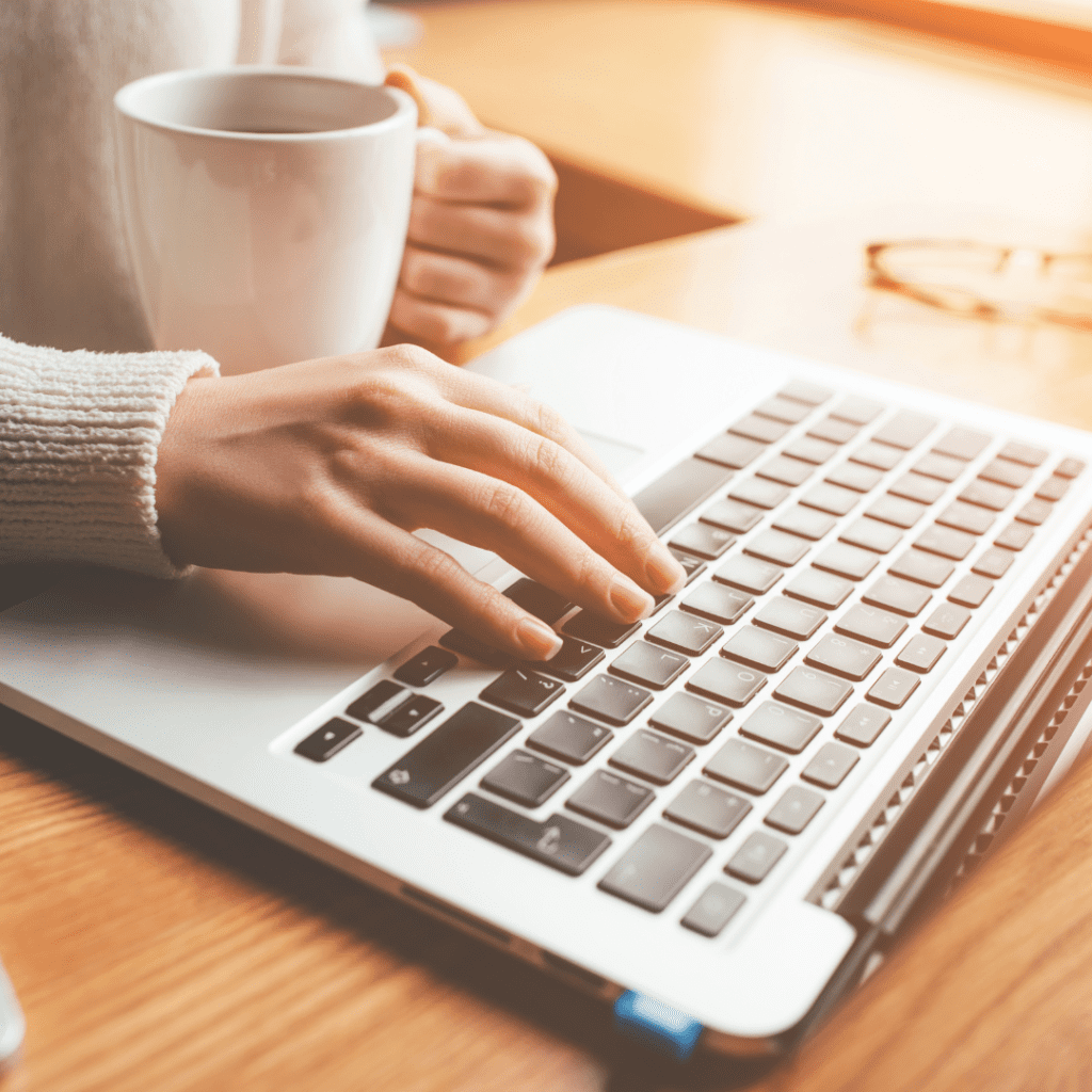 Woman working on a laptop with coffee in other hand