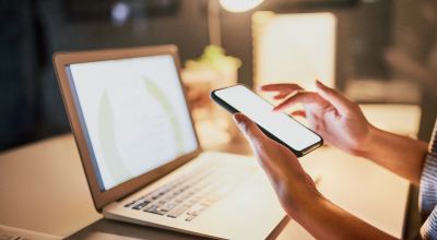 Woman working on phone with laptop open on the desk